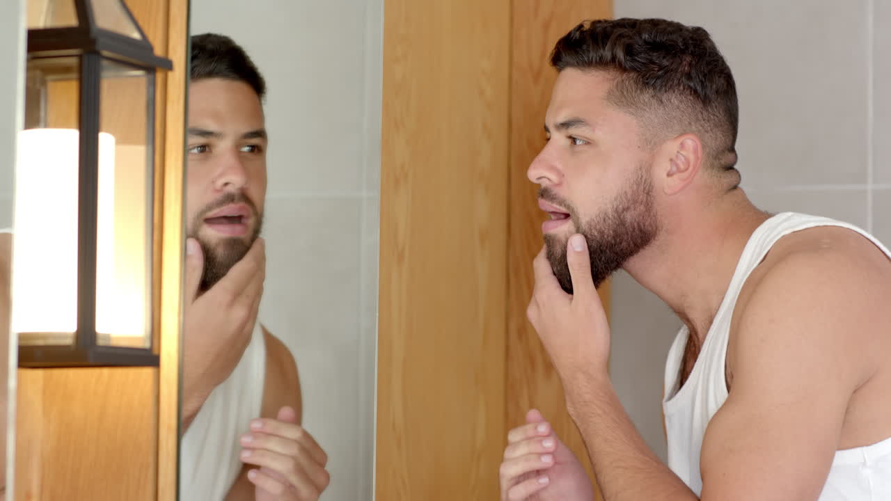Grooming beard, man examining reflection in bathroom mirror at home