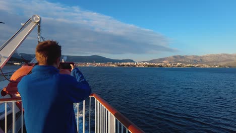 Ein-Tourist-Nimmt-Auf-Seinem-Handy-Ein-Video-Von-Der-Küste-Im-Offenen-Wasser-Auf,-Während-Das-Boot-Von-Split-Zur-Insel-Vis-In-Kroatien-In-Der-Adria-Segelt