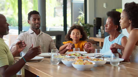 multi-generation family joining hands and saying prayer before meal at home