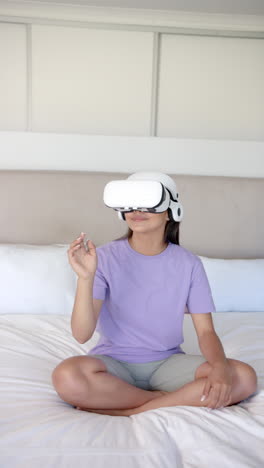 vertical video: using vr headset, woman sitting cross-legged on bed, interacting with virtual world