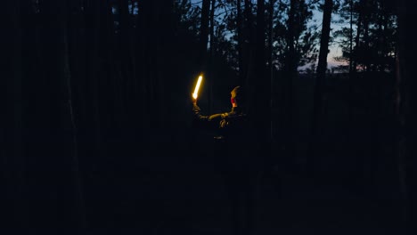 aventurero con mochila y luz de antorcha camina por el bosque oscuro buscando la oscuridad por la noche