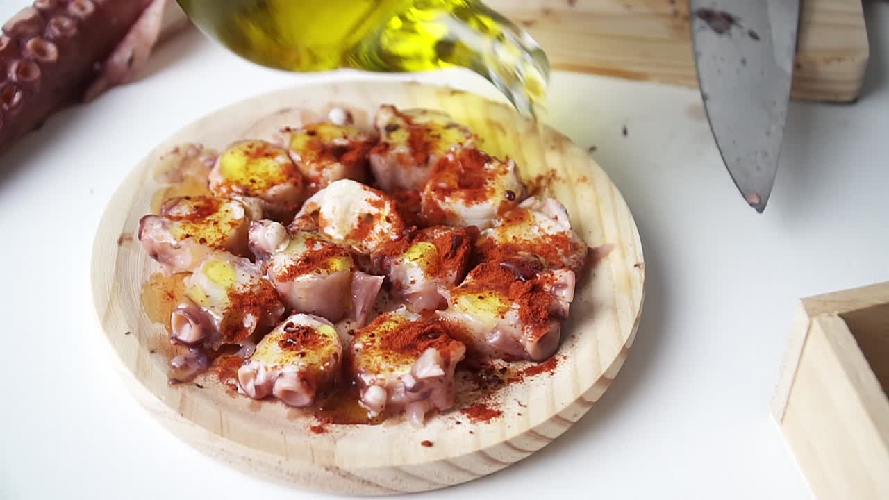 pulpo sazonado con pimentón, vertiendo un poco de aceite de oliva para templar y prepararlo para cocinar, sobre una tabla de cortar de madera y una mesa blanca