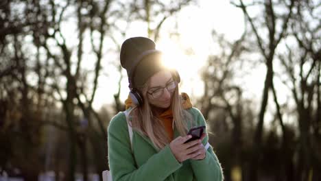 happy woman dance in winter park, listening to music on the phone using headphones