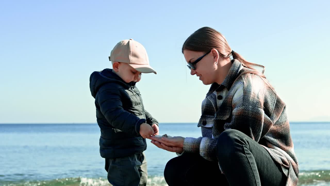 Madre felice a passeggio con il figlio in riva al mare. La madre passeggia con il figlio sul litorale in autunno. L'aria di mare è benefica per il bambino e la madre.