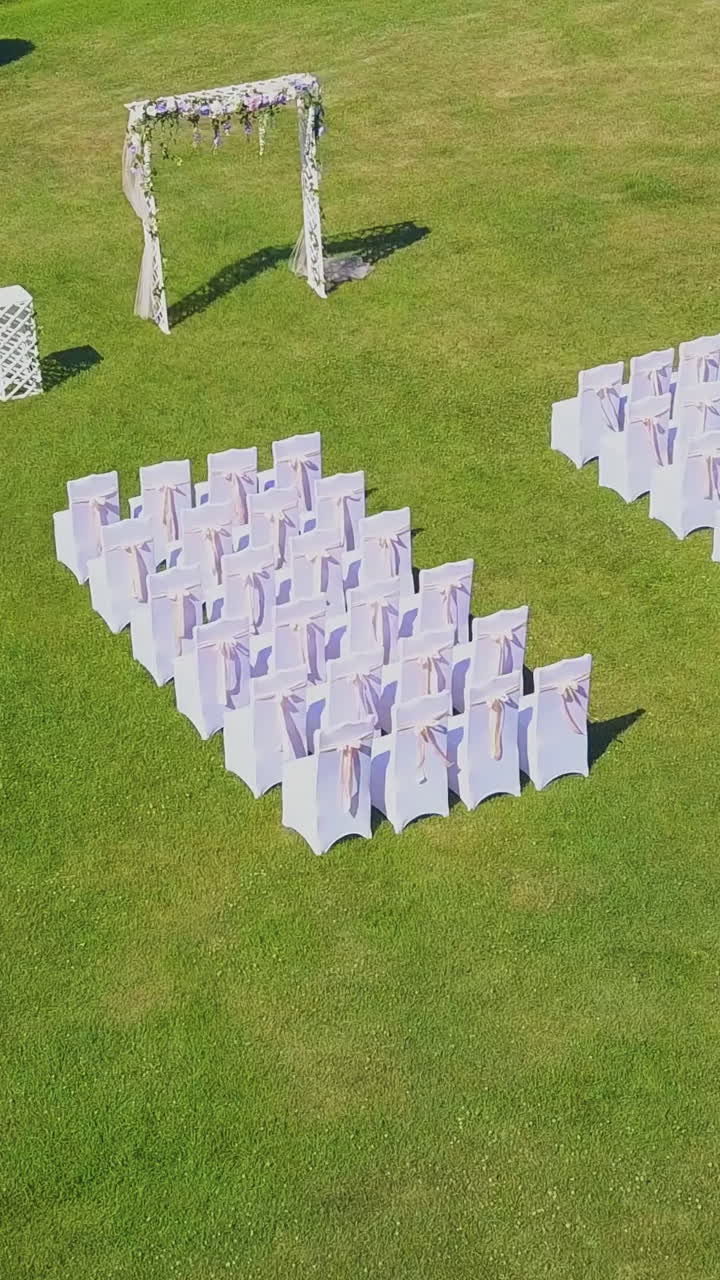 wedding ceremony site with arch and white chairs on green grass lawn on sunny autumn day aerial view