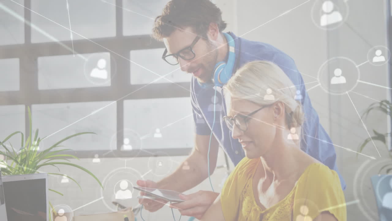 Colleagues leaning over desk collaborating on tablet in technology office, showing network icons