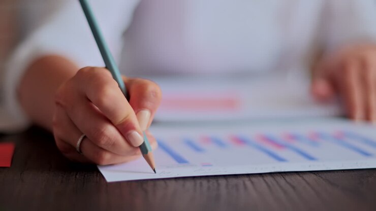 Donna che scrive su un foglio con un grafico su una scrivania, in un ufficio