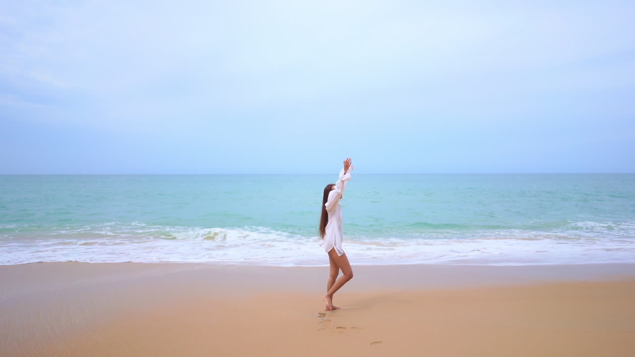 해변에 있는 젊은 여성은 팔을 들고 수평선을 바라보며 자유 개념을 표현합니다.