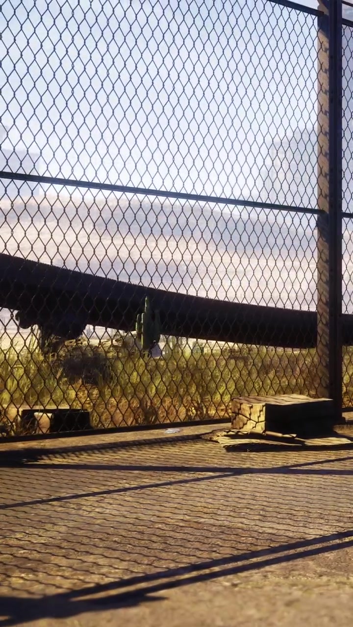 Un treno passa accanto a una recinzione al tramonto, vicino a un binario ferroviario.