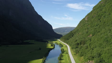 aerial shot of a valley with a road, a serene river, and lush green hills extending into the horizon.