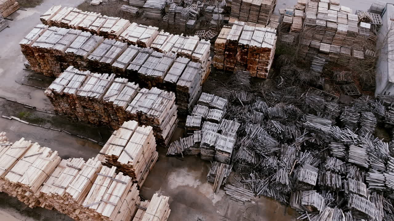 Slow aerial footage of a large industrial yard that is filled with piles of pallet wood.