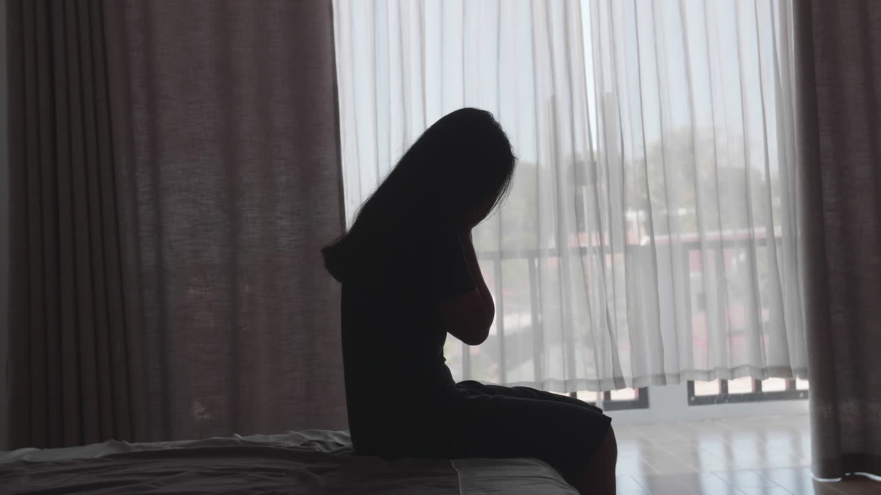 Silhouette Of Sad And Depressed Women Sitting On Bed