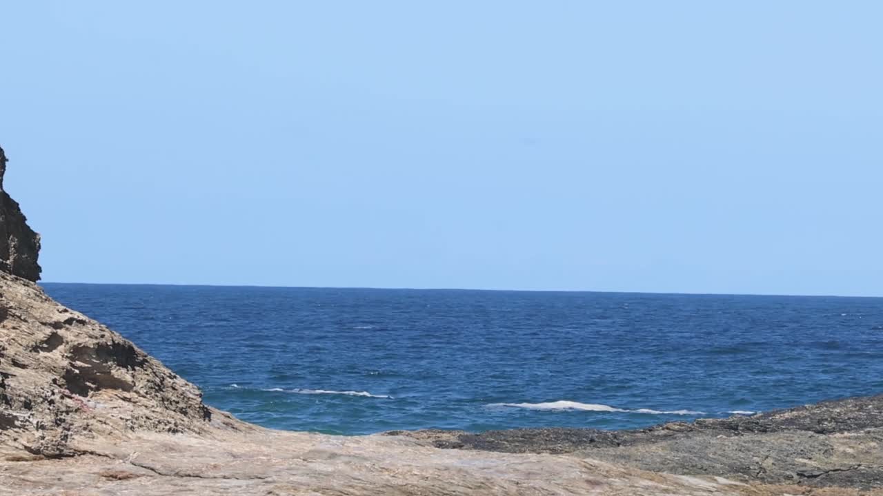 A serene view of the ocean framed by a rugged rocky cliff under a clear blue sky.