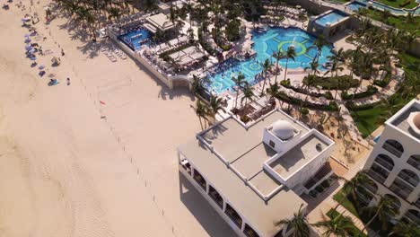 An-aerial-drone-flies-along-the-beach-of-Cabo-San-Lucas-above-the-outdoor-pools-of-the-resorts-below