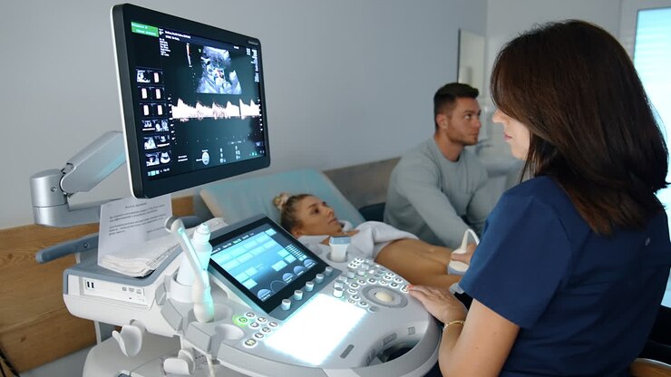 Obstetrician works on modern equipment for sonography. Dark-haired doctor checks up the pregnancy development of a Caucasian woman. Man at backdrop.