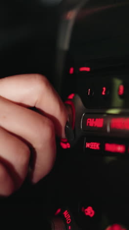 vista en primera persona de la mano de una mujer girando el botón de la radio fm dentro de un coche por la noche. el tablero de instrumentos está iluminado con luces rojas