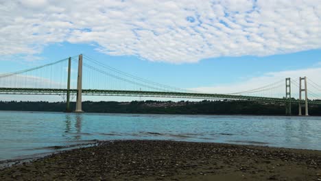 time lapse, hyperlapse, high stratus clouds streaming over puget sound and the tacoma narrows bridge, zoom out to a sand and pebble beach