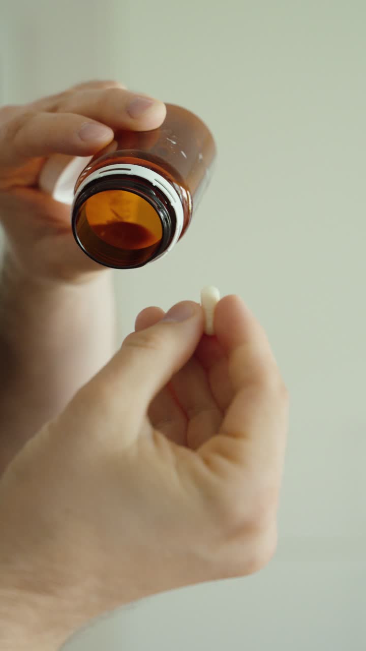 Primo piano di un flacone di pillole con l'ultima compressa che cade in una mano, a simboleggiare il dosaggio, la routine dei farmaci e l'esaurimento.