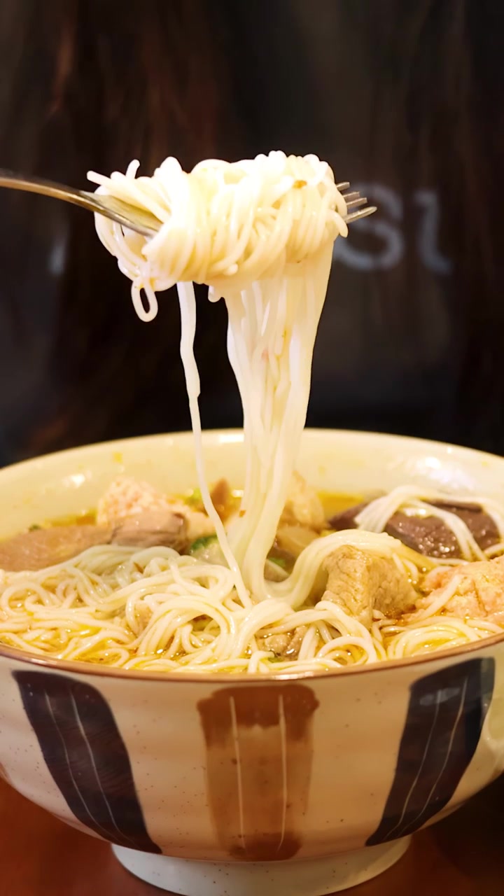 Una persona solleva spaghetti di riso bianchi con una forchetta da una tradizionale ciotola di ceramica per zuppa