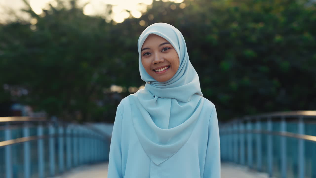 Portrait of a Smiling Young Muslim Woman in a Light Blue Hijab on a Bridge
