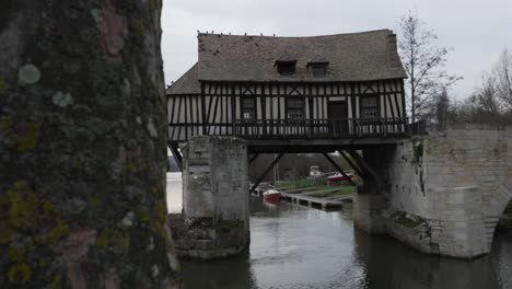 push past cinematic reveal behind tree of small house mill built above river on concrete structures