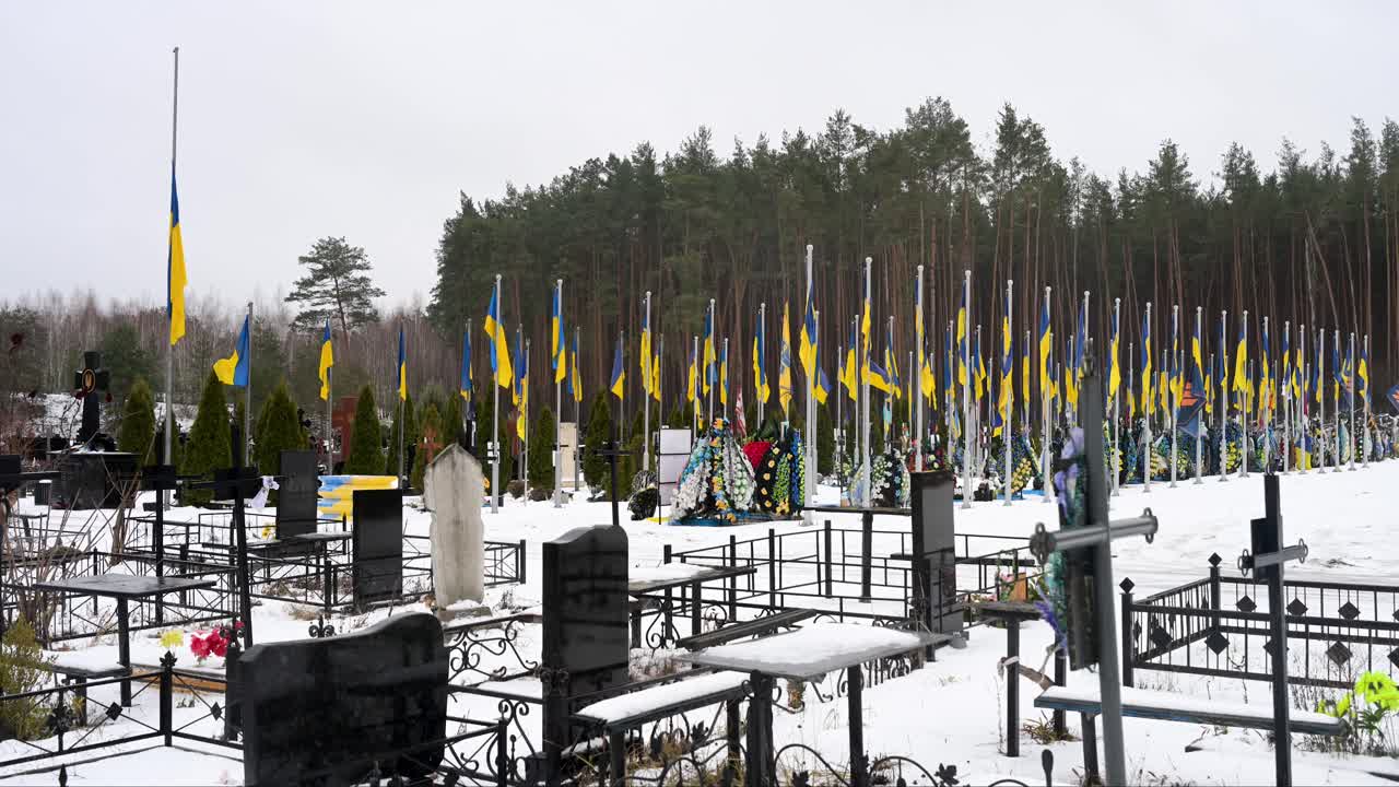 Wide shot of Irpin cemetery on a winter day, with Ukrainian flags standing over soldiers' graves, honoring those who fell in the Ukraine-Russia war. Snow-covered ground adds to the solemn atmosphere.