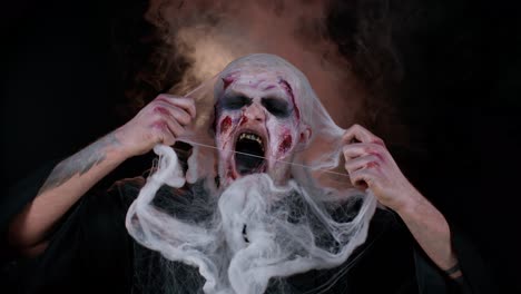 sinister man in costume of halloween crazy zombie with bloody wounded scars face screaming, shouting