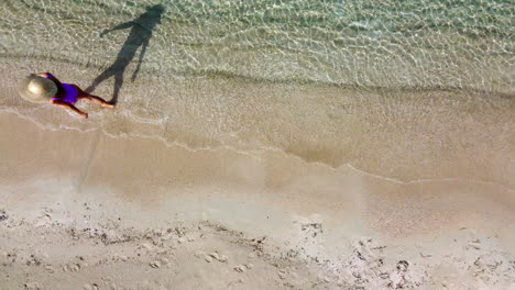 A-woman-in-a-pink-swimsuit-and-straw-hat-walks-along-a-sandy-beach