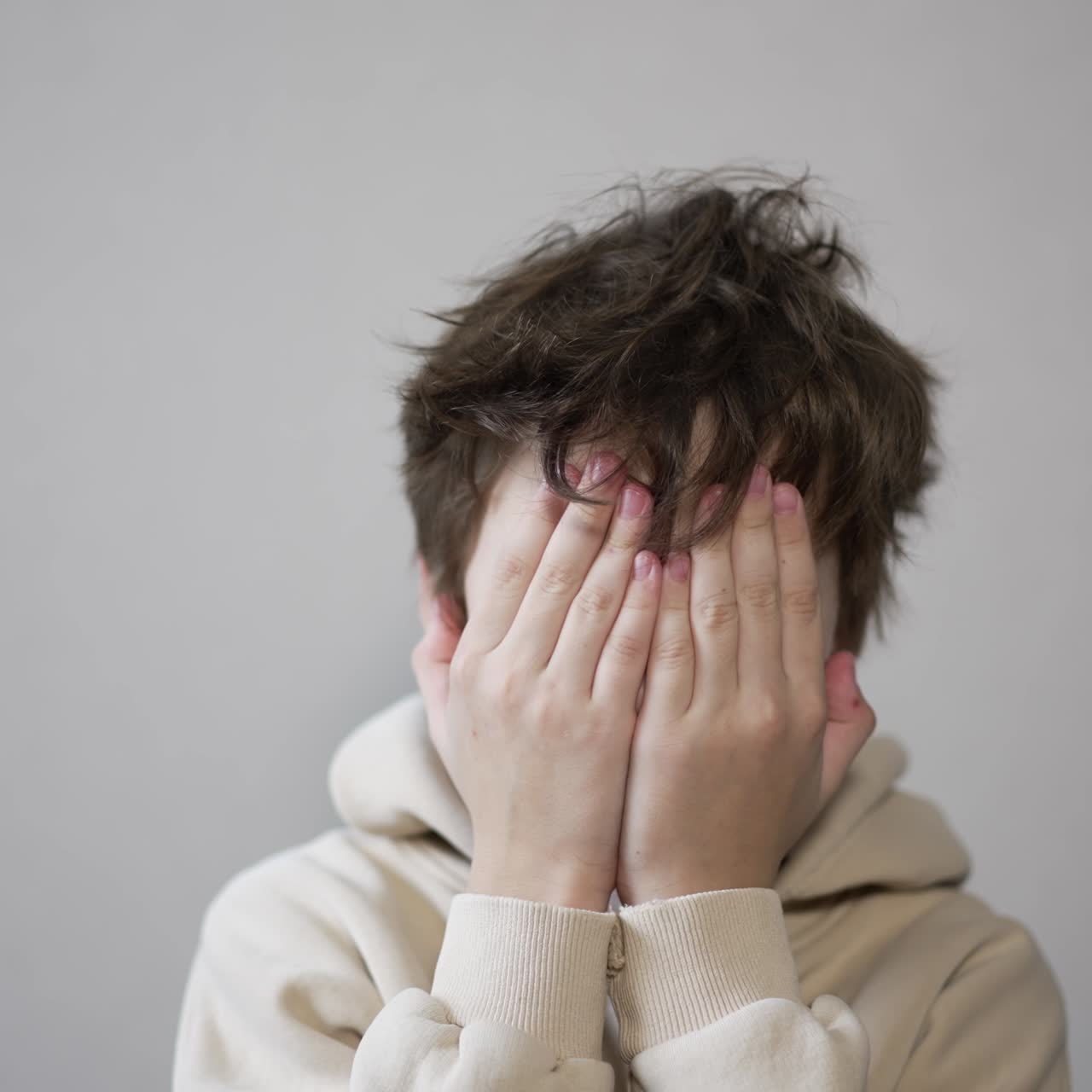 Handsome Caucasian boy posing in front of camera. Kid puts his hands on face, rubs his eyes and then stretches arms to the sides lazily