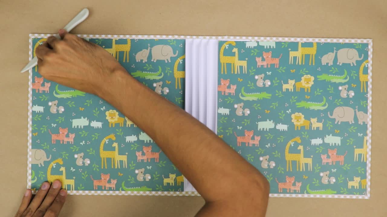 Attaccare carta di sfondo a tema animale per uno scrapbook per neonati.