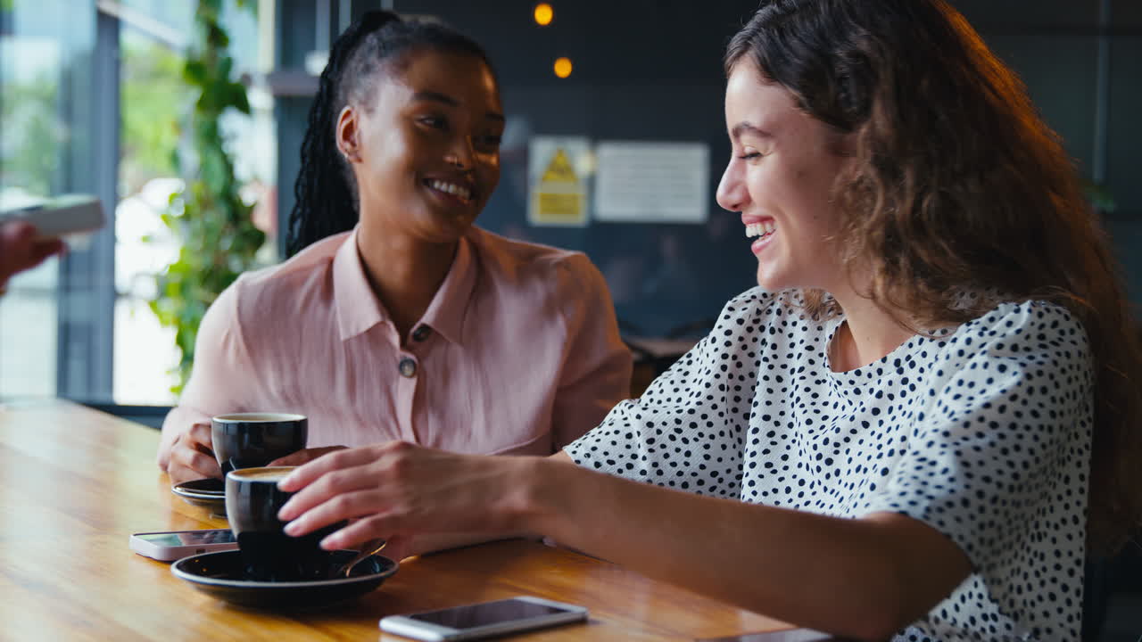 Woman In Coffee Shop Paying Bill With Contactless Mobile Phone Payment