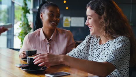 woman in coffee shop paying bill with contactless mobile phone payment