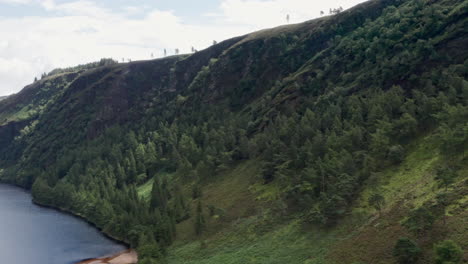 Toma-Aérea-Que-Orbita-La-Montaña-En-El-Lago-Superior-Glendalough-En-El-Parque-Nacional-De-Las-Montañas-Wicklow-En-Irlanda