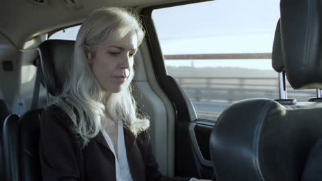 gray haired businesswoman working on laptop in car