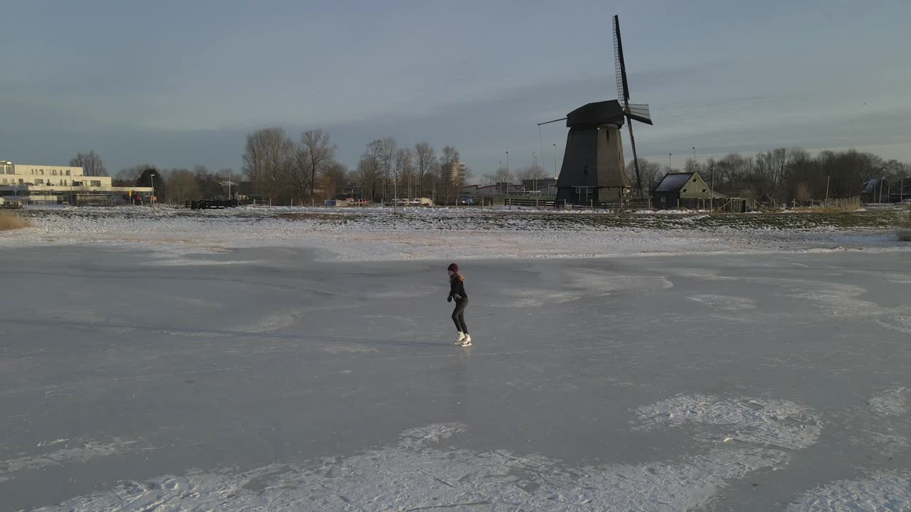 Vista aerea di un mulino a vento con ghiaccio invernale scintillante all'alba ad Alkmaar, Paesi Bassi, con una splendida illuminazione all'alba, atmosfera serena, riprese drone di alta qualità che evidenziano la bellezza naturale.