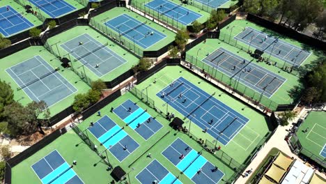 Pickleball-tournament-event-with-many-courts-of-players,-aerial-flyover-on-bright-day