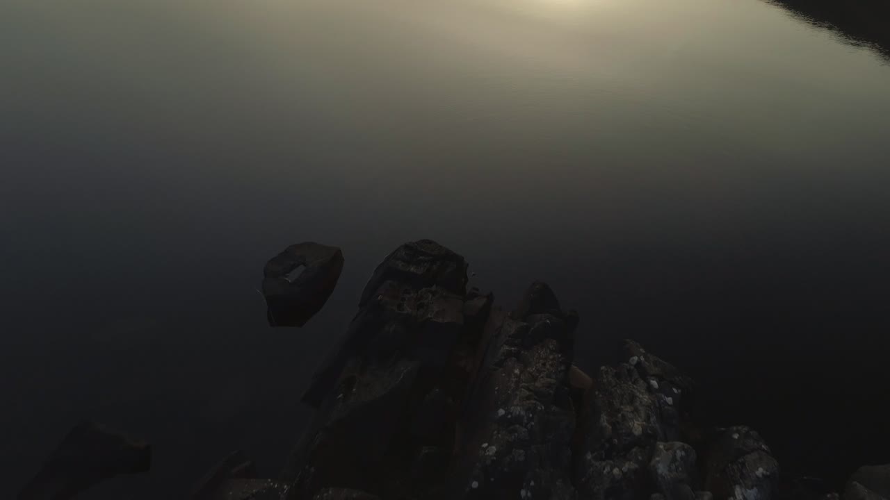 антенна человека, стоящего на камнях на озере в эпическом потрясающий закат отражение на поверхности воды в каньоне силуэт - наклон вверх медленно раскрытия выстрел