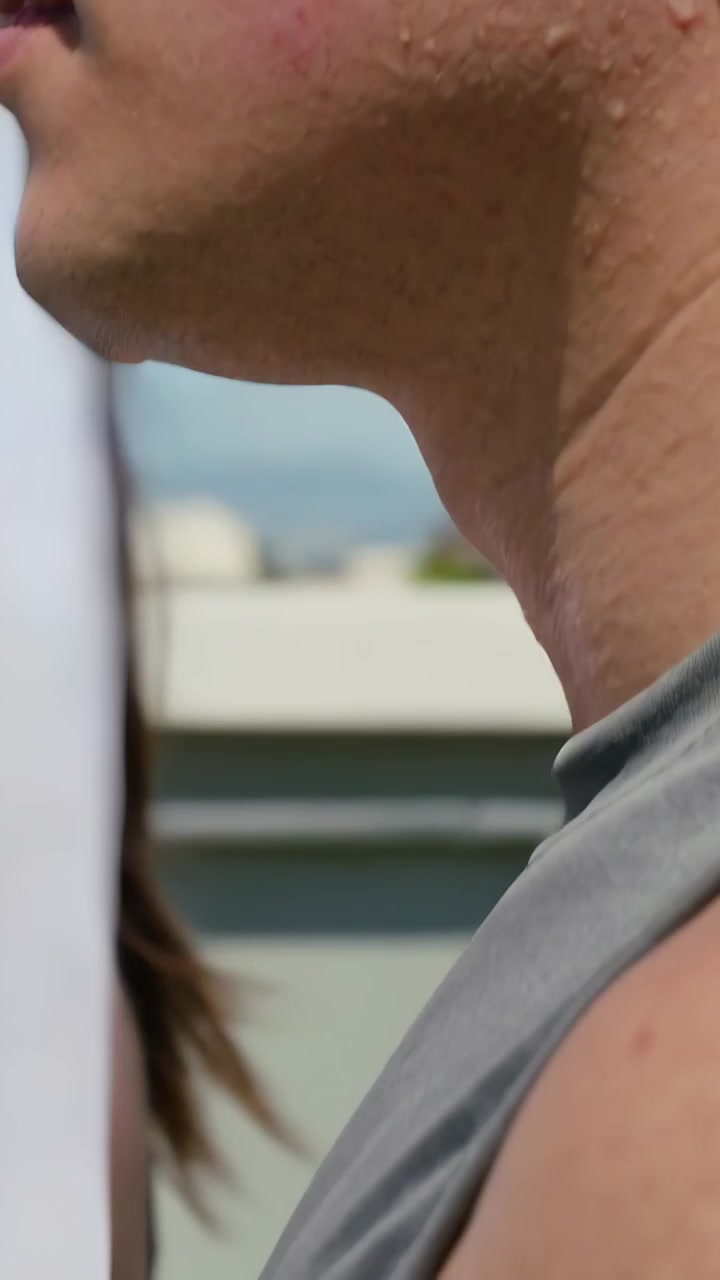 Video verticale: Mostra un uomo con una canotta grigia che suda su un tetto, mentre strisce di carta passano facendogli girare la testa.