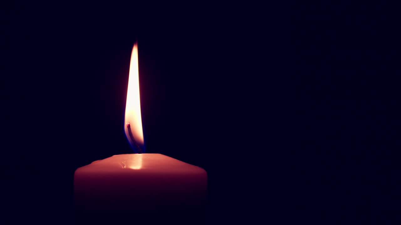 singola grande fiamma di candela gialla si accende e si spegne, isolata su uno sfondo nero