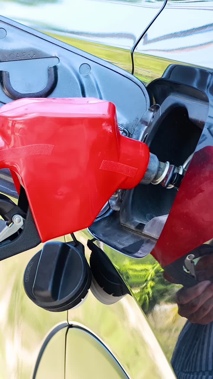 Una persona inserisce una pistola rossa per il carburante nel serbatoio dell'auto presso una stazione di servizio all'aperto, in pieno giorno.