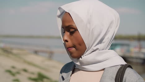 sorrowing black woman with headscarf stands on embankment