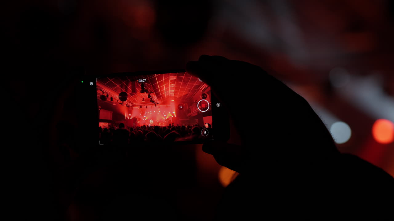 Mano che Tiene lo Smartphone e Filma un Vivace Concerto Musicale