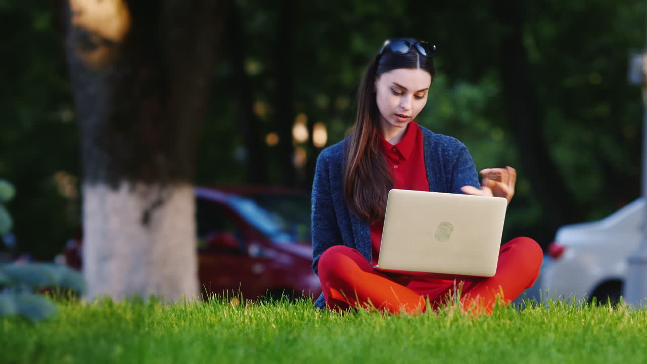 una estudiante sentada en el césped del parque usa un video hd de una laptop