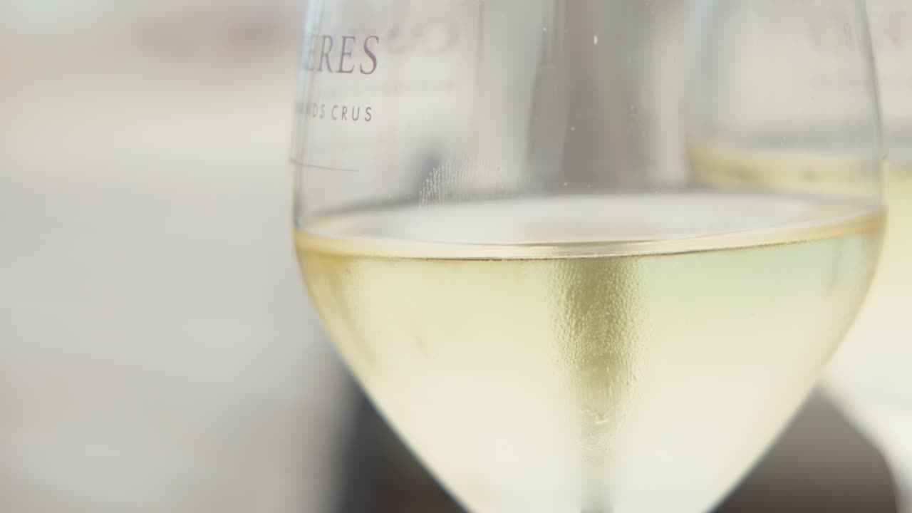 Due calici di vino bianco illuminati dalla luce tenue del giorno, messa a fuoco superficiale, terrazza all'aperto, atmosfera estiva rilassata
