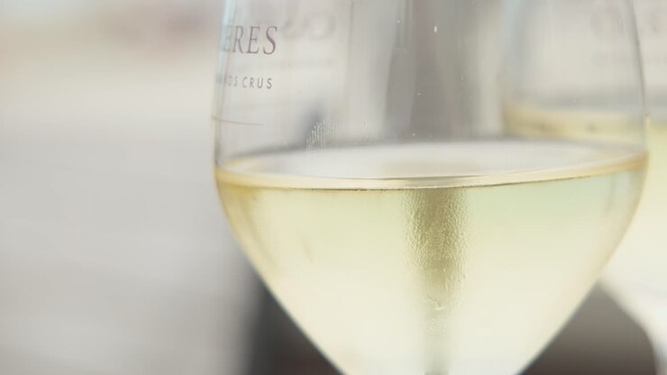 Due calici di vino bianco illuminati dalla luce tenue del giorno, messa a fuoco superficiale, terrazza all'aperto, atmosfera estiva rilassata