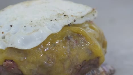 macro primer plano de una hamburguesa con queso en la parrilla de un restaurante con un huevo frito encima mientras se cocina