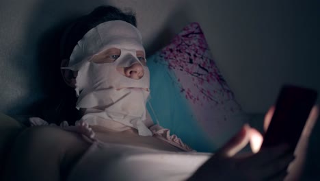 girl in pink top with white skincare mask lies on pillow