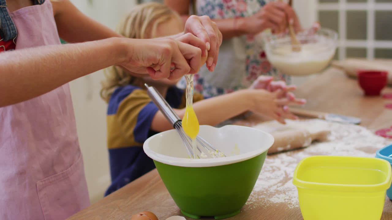Midsection of caucasian mother in kitchen baking son and daughter breaking egg into a bowl