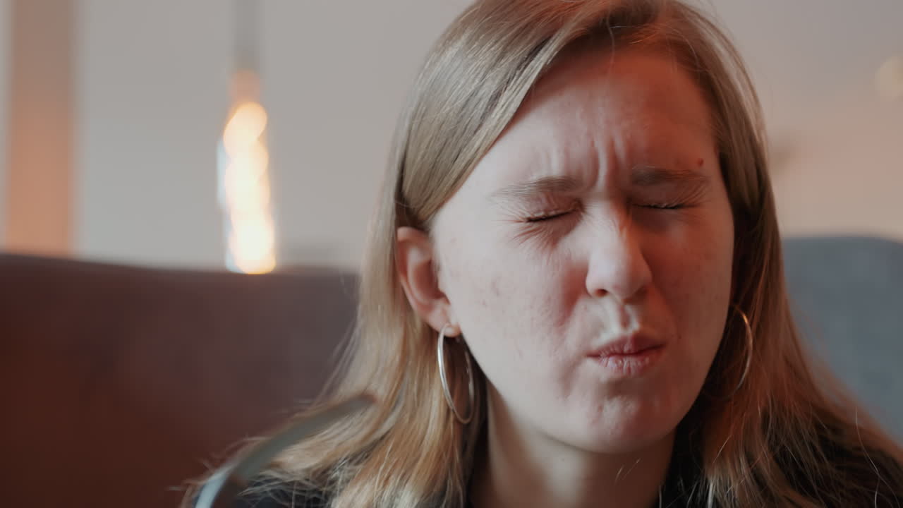 Donna caucasica che fa una smorfia per un boccone amaro, ambiente interno intimo con il caldo bagliore di una lampada, primo piano di espressioni facciali, orecchino a cerchio visibile, reazione emotiva e onesta al cibo, ritratto spontaneo e accogliente.