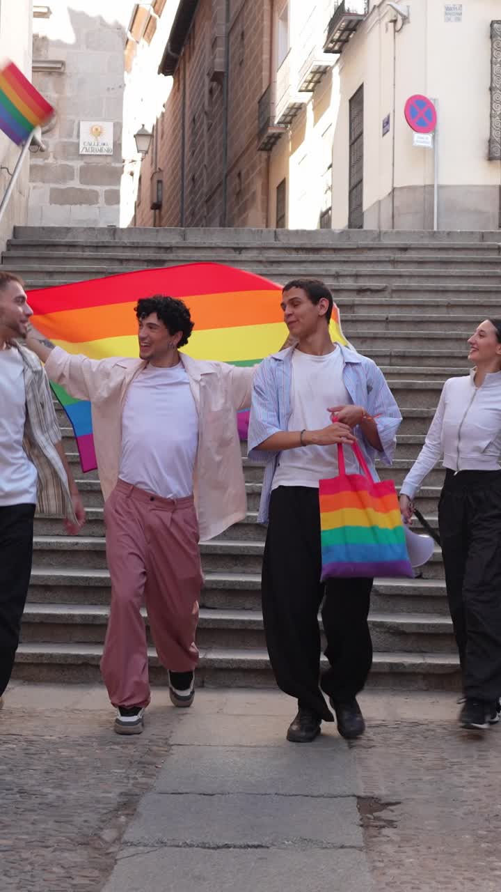 Jóvenes alegres bajando escaleras de la ciudad con una bandera del orgullo arcoíris.